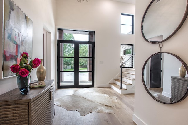 entryway with french doors, light hardwood / wood-style flooring, plenty of natural light, and a high ceiling