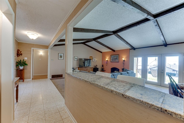 kitchen with lofted ceiling with beams, light stone countertops, a textured ceiling, and french doors