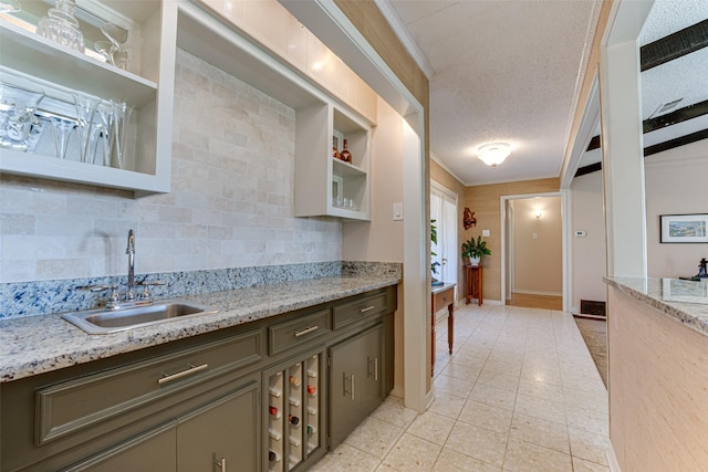 kitchen featuring sink, backsplash, light stone counters, crown molding, and a textured ceiling