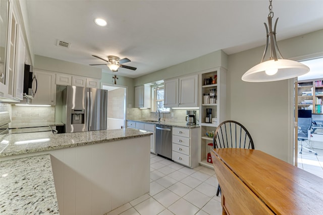 kitchen with white cabinets, hanging light fixtures, light tile patterned floors, light stone counters, and stainless steel appliances