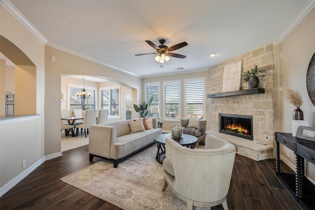 living room with dark hardwood / wood-style flooring, crown molding, a stone fireplace, and ceiling fan with notable chandelier