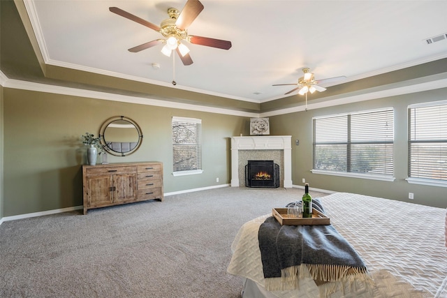 carpeted bedroom with a tiled fireplace, ceiling fan, ornamental molding, and a raised ceiling