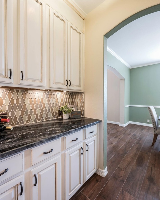 kitchen featuring tasteful backsplash, dark stone countertops, white cabinets, crown molding, and dark wood-type flooring