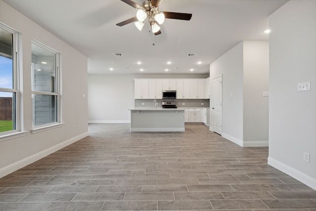 kitchen with an island with sink, sink, white cabinets, light hardwood / wood-style floors, and stainless steel appliances