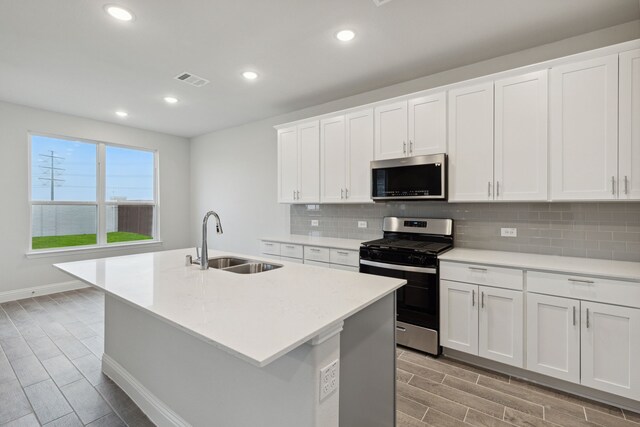 kitchen with a center island with sink, white cabinets, sink, decorative backsplash, and stainless steel appliances