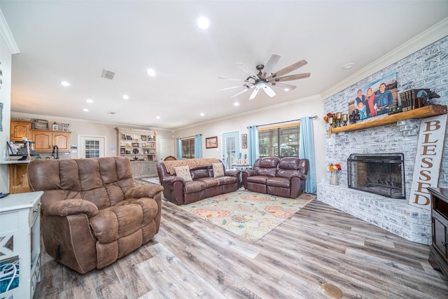 living room with crown molding, ceiling fan, a brick fireplace, and light hardwood / wood-style flooring