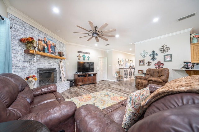 living room featuring ceiling fan, ornamental molding, a stone fireplace, and light wood-type flooring