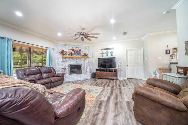 living room with ornamental molding, a large fireplace, ceiling fan, and light wood-type flooring