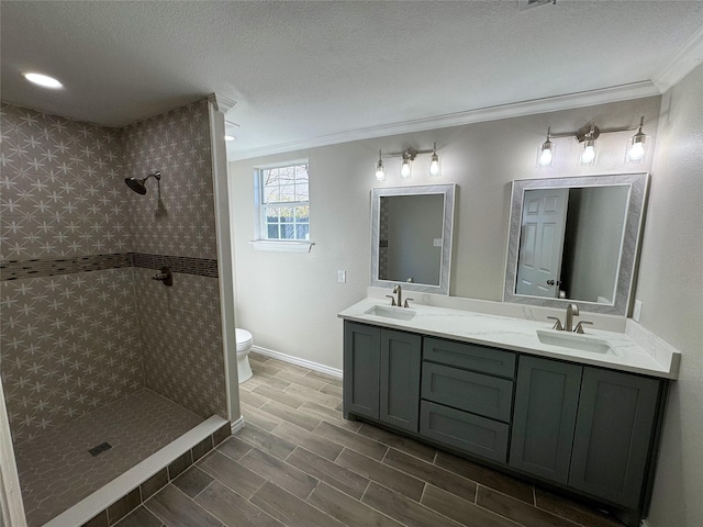 bathroom with crown molding, tiled shower, vanity, and toilet