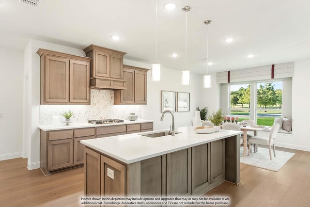 kitchen featuring light wood-type flooring, backsplash, sink, pendant lighting, and a center island with sink