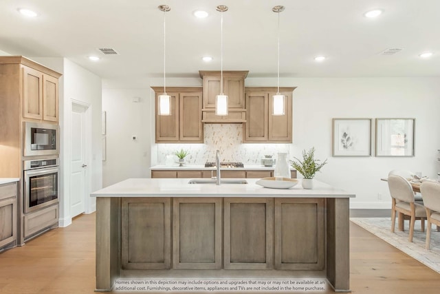 kitchen featuring black microwave, light hardwood / wood-style flooring, oven, decorative light fixtures, and a center island with sink