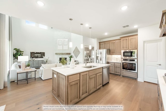 kitchen with stainless steel appliances, sink, a center island with sink, light hardwood / wood-style floors, and hanging light fixtures