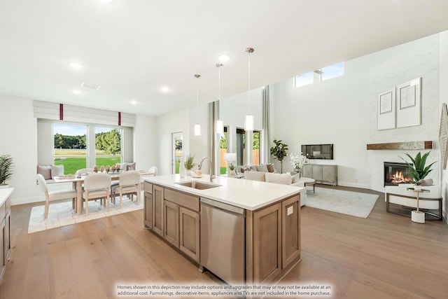 kitchen featuring pendant lighting, a center island with sink, sink, stainless steel dishwasher, and a fireplace