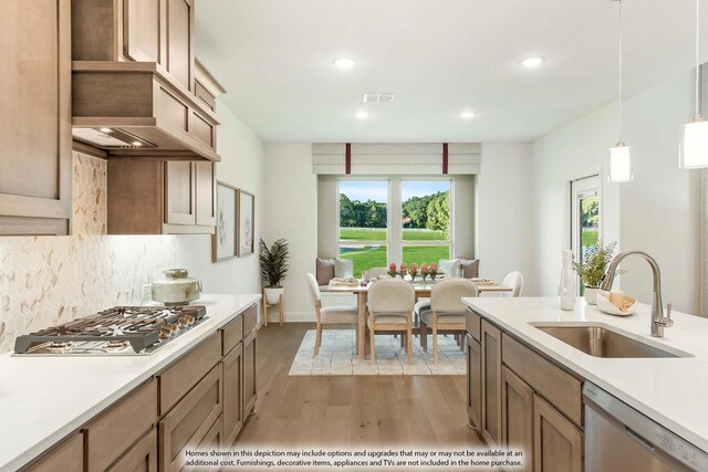 kitchen with pendant lighting, backsplash, sink, appliances with stainless steel finishes, and light hardwood / wood-style floors