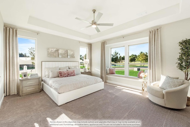 bedroom featuring ceiling fan, light colored carpet, and a tray ceiling