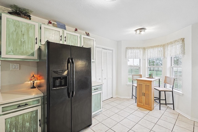 kitchen with light tile patterned flooring, black fridge with ice dispenser, a textured ceiling, and a wealth of natural light