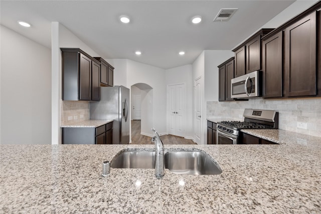 kitchen featuring light stone counters, sink, dark brown cabinets, and appliances with stainless steel finishes