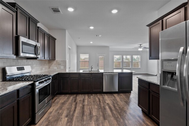 kitchen featuring sink, stainless steel appliances, dark wood-type flooring, backsplash, and kitchen peninsula