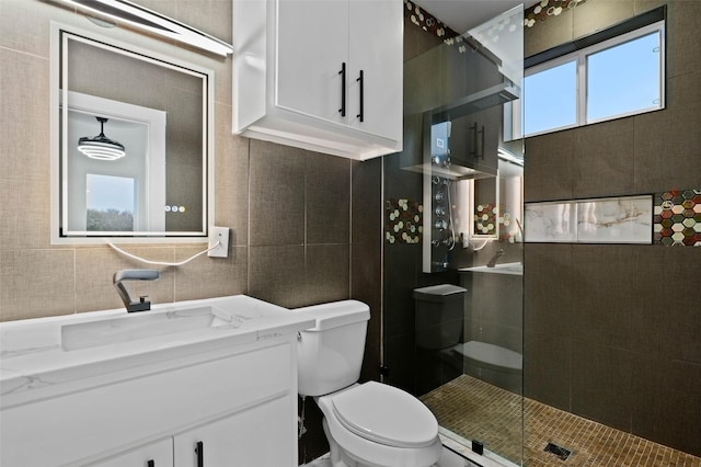 bathroom with a walk in shower, vanity, toilet, and tile walls