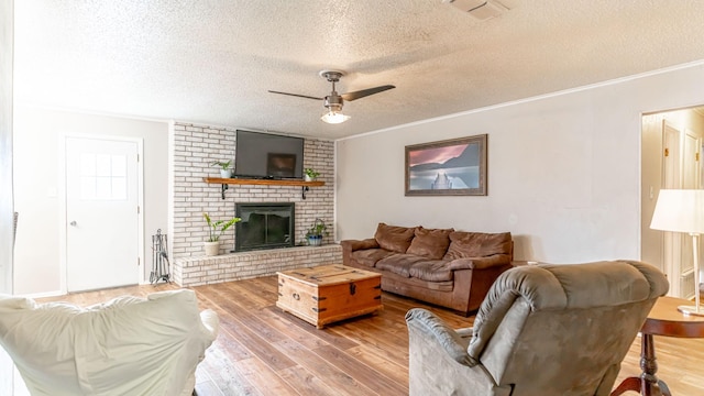 living room with a textured ceiling, ceiling fan, crown molding, hardwood / wood-style flooring, and a fireplace