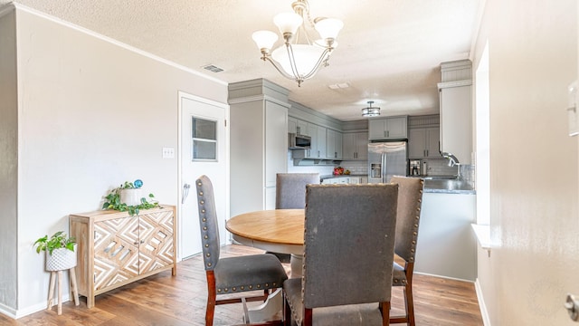 dining area with sink, an inviting chandelier, dark hardwood / wood-style flooring, crown molding, and a textured ceiling