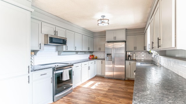 kitchen featuring hardwood / wood-style floors, sink, dark stone countertops, tasteful backsplash, and stainless steel appliances