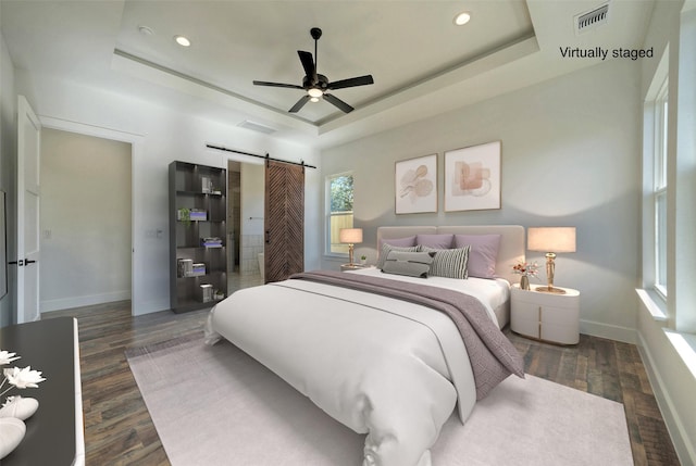 bedroom featuring a tray ceiling, dark wood-type flooring, and a barn door