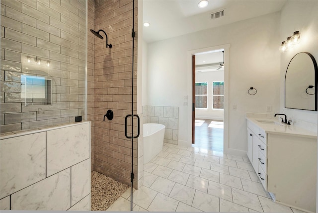 bathroom with ceiling fan, vanity, shower with separate bathtub, and tile walls