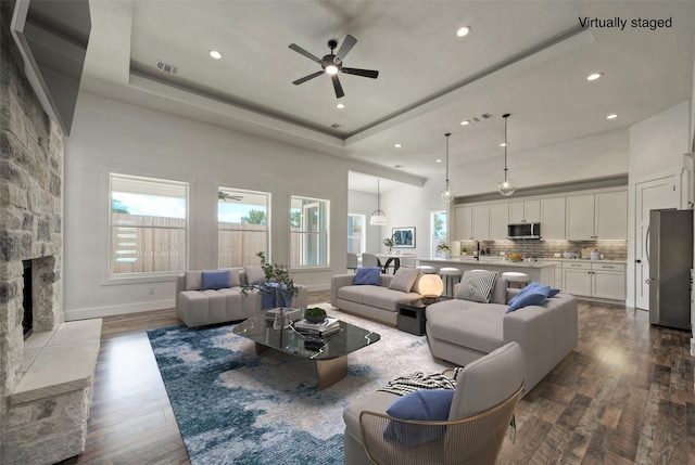 living room with hardwood / wood-style flooring, a stone fireplace, a raised ceiling, and a high ceiling