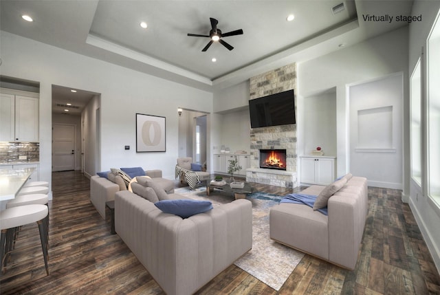 living room with a fireplace, a towering ceiling, dark wood-type flooring, and a raised ceiling