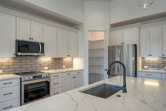 kitchen featuring stainless steel appliances, light stone countertops, sink, and white cabinets