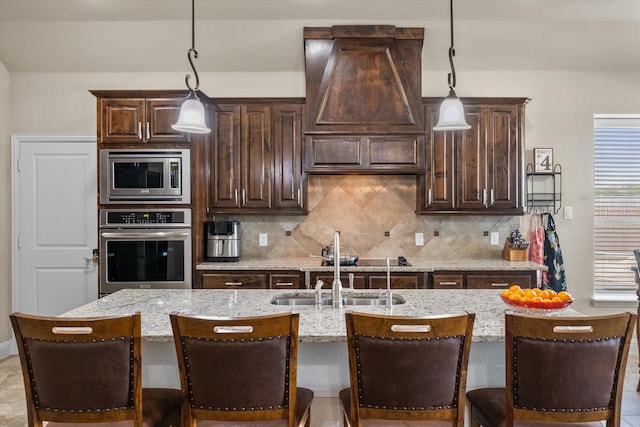 kitchen featuring dark brown cabinetry, a center island with sink, stainless steel appliances, and decorative light fixtures