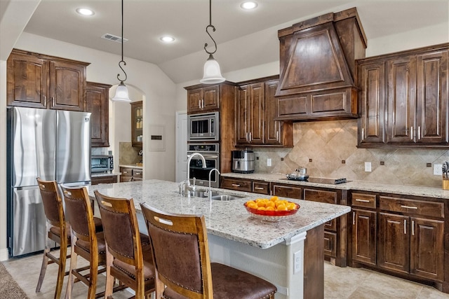 kitchen with stainless steel appliances, dark brown cabinets, a center island with sink, and decorative light fixtures