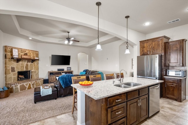 kitchen with arched walkways, an island with sink, open floor plan, stainless steel appliances, and a sink