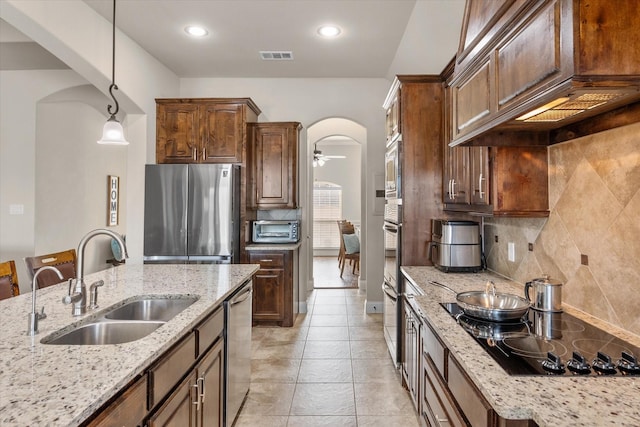 kitchen with arched walkways, light stone counters, stainless steel appliances, a sink, and decorative light fixtures