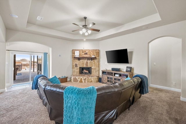 living room featuring a raised ceiling, carpet flooring, and a stone fireplace