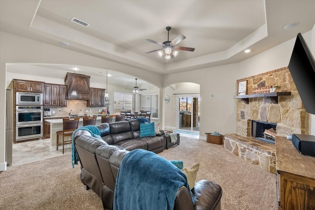 living area with visible vents, arched walkways, a raised ceiling, light colored carpet, and a stone fireplace