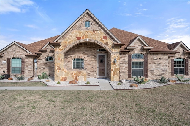 french provincial home with roof with shingles, a front lawn, and brick siding