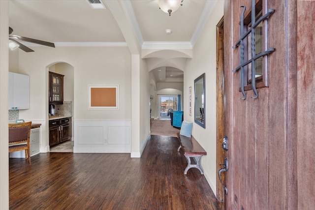 entryway featuring ceiling fan, arched walkways, visible vents, ornamental molding, and dark wood-style floors