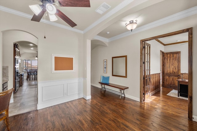 spare room featuring arched walkways, a wainscoted wall, visible vents, dark wood-style floors, and crown molding