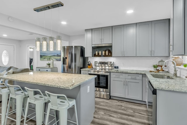 kitchen featuring appliances with stainless steel finishes, light stone counters, sink, a center island, and gray cabinets