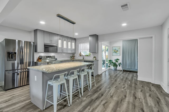 kitchen featuring appliances with stainless steel finishes, a breakfast bar, pendant lighting, a center island, and gray cabinets