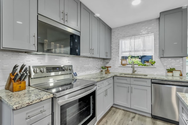 kitchen with gray cabinetry, sink, light stone countertops, light wood-type flooring, and stainless steel appliances