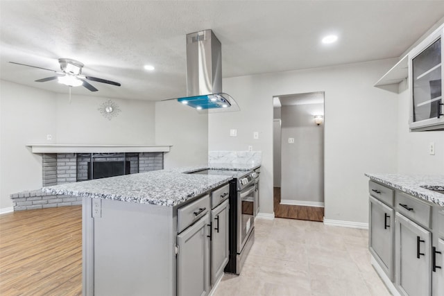 kitchen featuring ceiling fan, ventilation hood, a textured ceiling, gray cabinets, and stainless steel stove