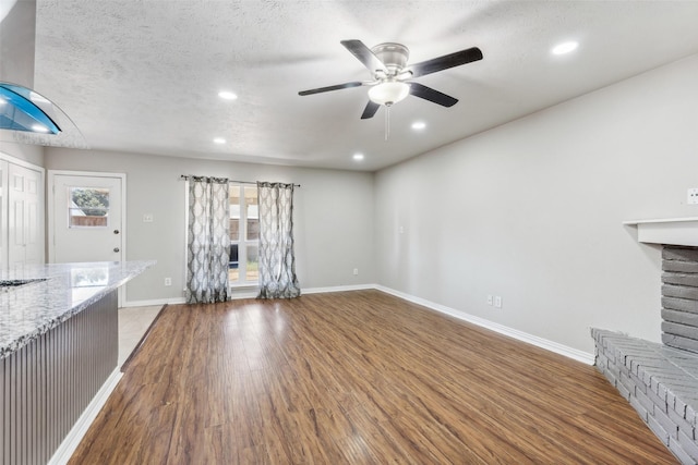 unfurnished living room with hardwood / wood-style floors, ceiling fan, a fireplace, and a textured ceiling