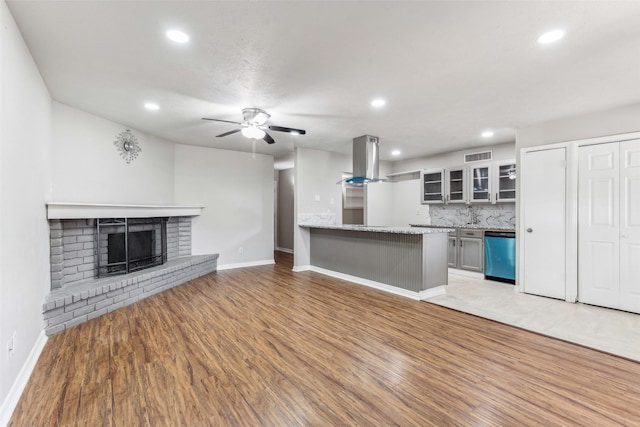 unfurnished living room featuring ceiling fan, light hardwood / wood-style floors, and a brick fireplace