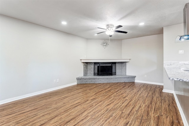 unfurnished living room featuring hardwood / wood-style flooring, ceiling fan, a textured ceiling, and a brick fireplace