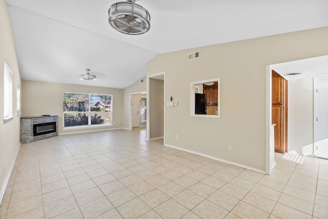 unfurnished living room with a stone fireplace, light tile patterned floors, and vaulted ceiling