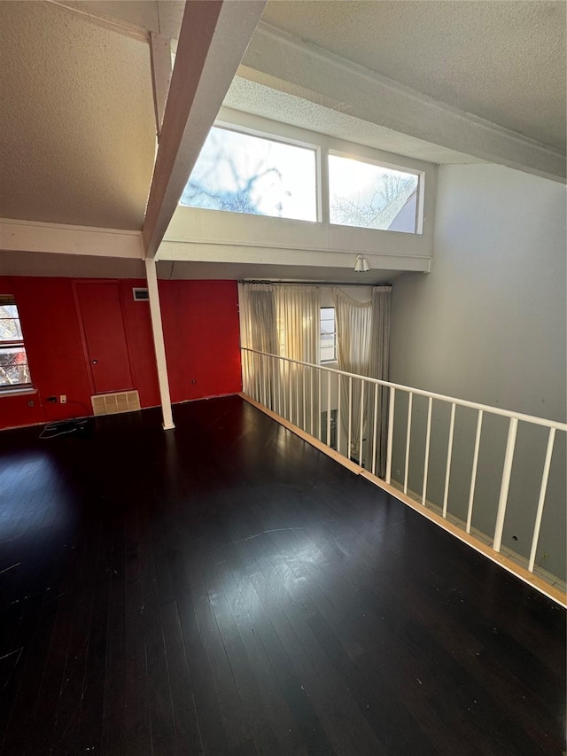 empty room featuring lofted ceiling with beams, a textured ceiling, and hardwood / wood-style flooring