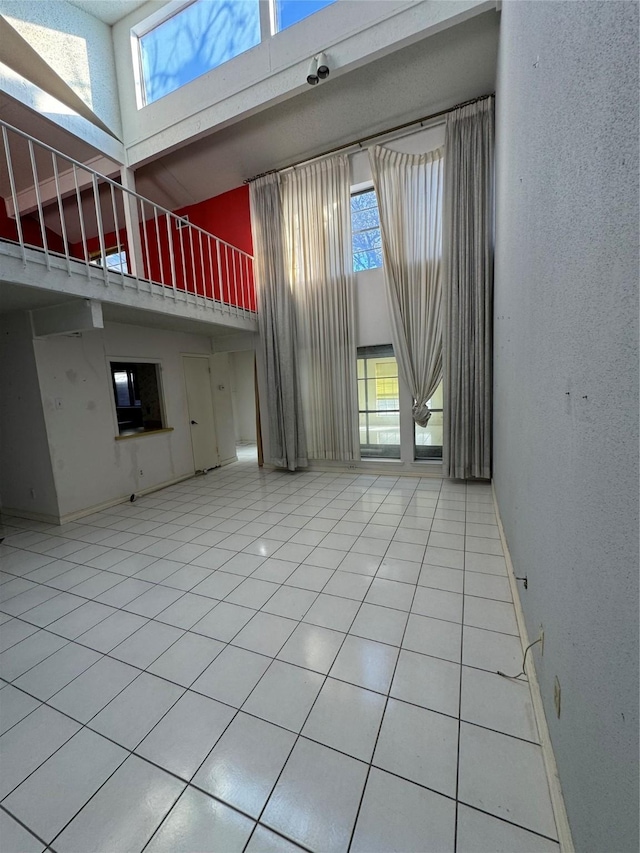 unfurnished living room featuring a towering ceiling, tile patterned floors, and a wealth of natural light